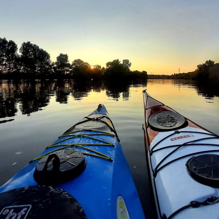 Zwei Kajaks schwimmen im ruhigen Wasser bei Sonnenuntergang.