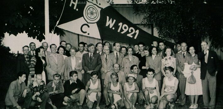 Gruppenfoto vor einem Zelt mit einer Aufschrift aus dem Jahr 1921, viele Personen in festlicher Kleidung.