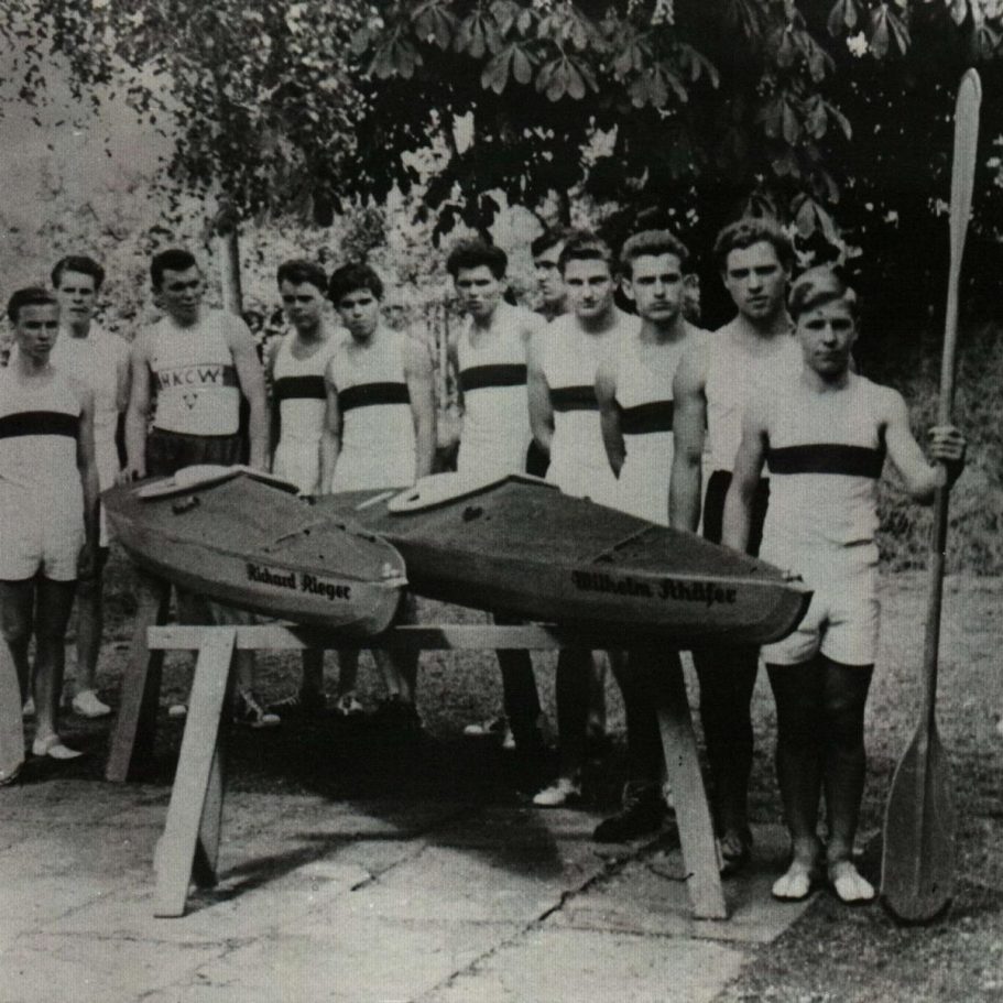 Gruppe von Männern in Sportkleidung mit Kajaks und Paddeln im Freien.