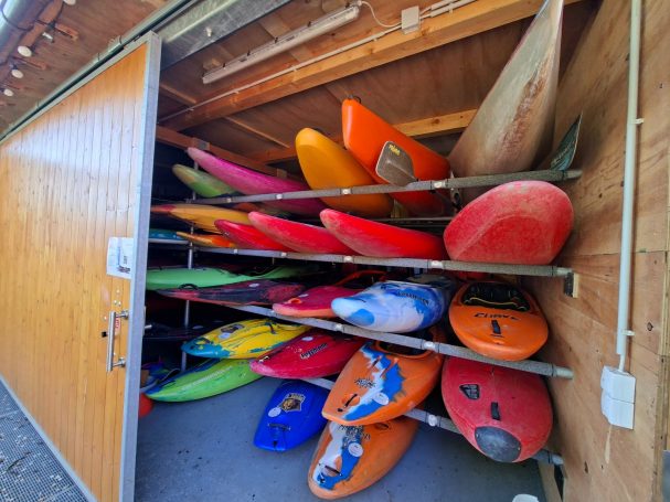 Bootsschuppen mit Wildwasser-Kajaks Bunte Kajaks in einem Holzschuppen auf Regalen gestapelt.