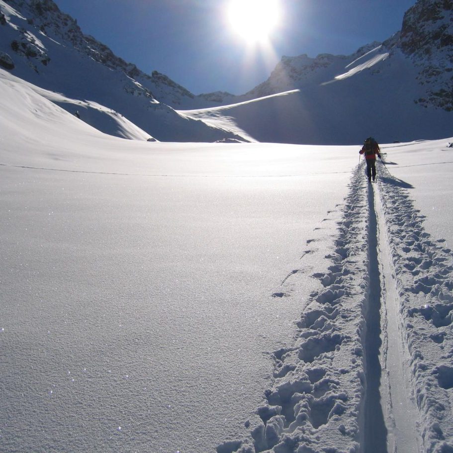 Ein Skiwanderer hinterlässt Spuren im frischen, glitzernden Schnee unter strahlender Sonne.