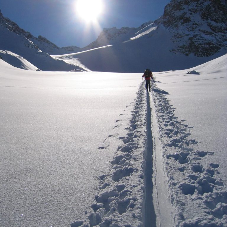 Ein Mensch wandert durch unberührten Schnee unter einem sonnigen Himmel in den Bergen.