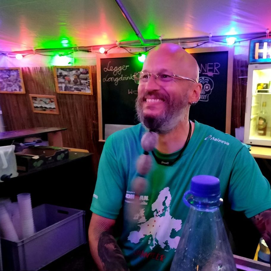 Mann mit Brille und Bart, lächelt in einer bunten, beleuchteten Bar.