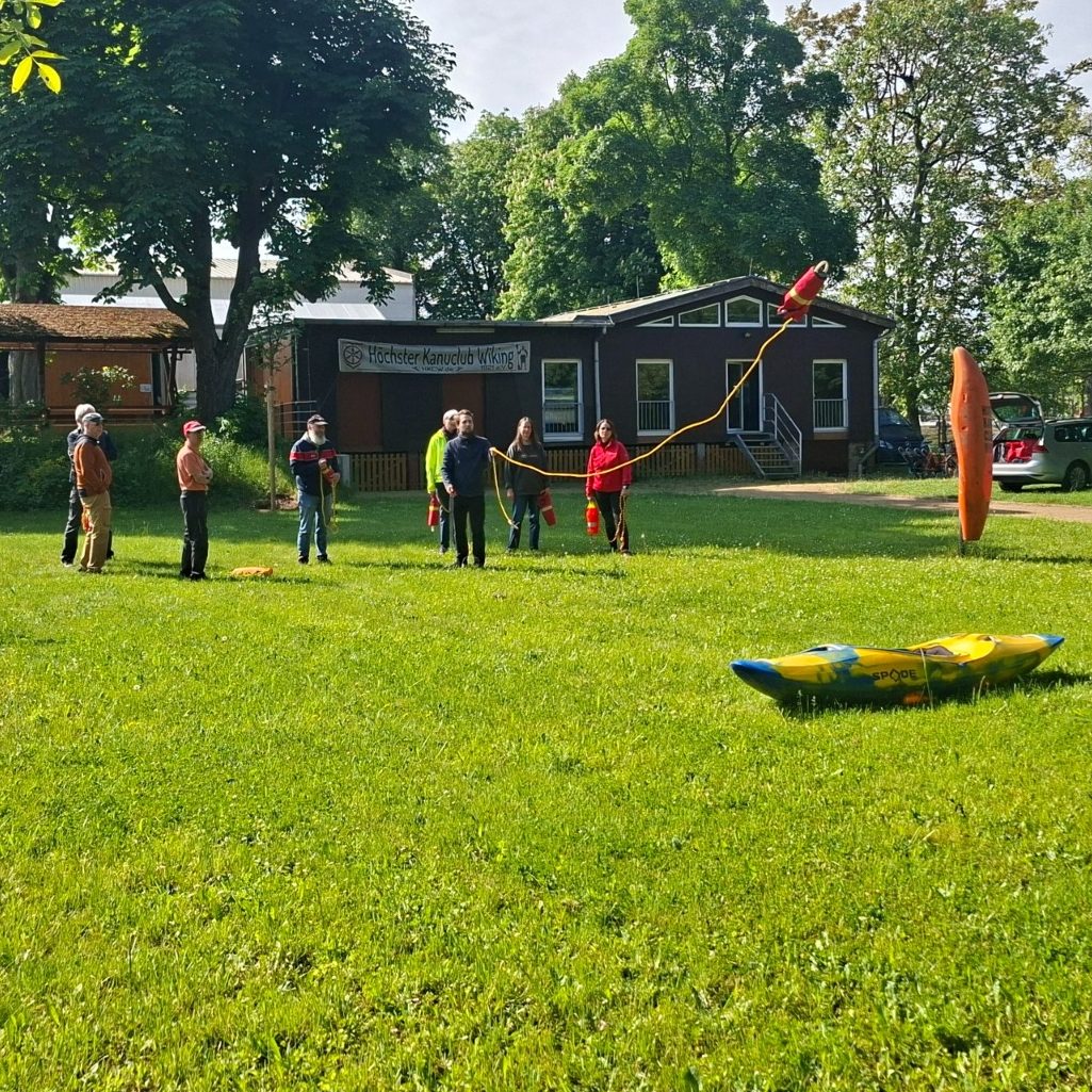Kajak-Sicherheitslehrgang: Wurfsacktraining Menschen üben Wurfsackwerfen im Freien auf einer grünen Wiese, umgeben von Bäumen und einem Gebäude.