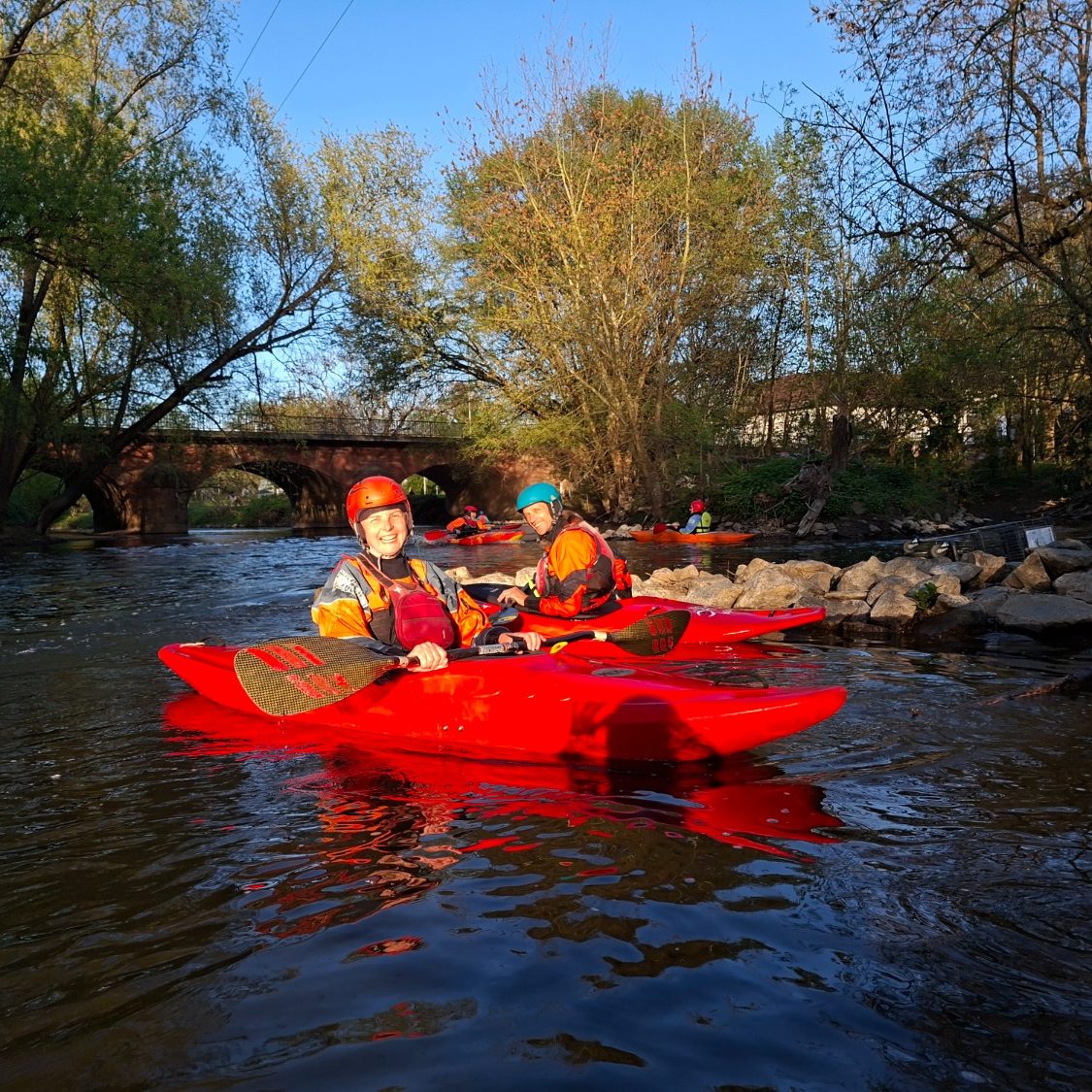 Training auf der Nidda Zwei Kajakfahrer in roten Kajaks auf einem ruhigen Fluss unter blauem Himmel.