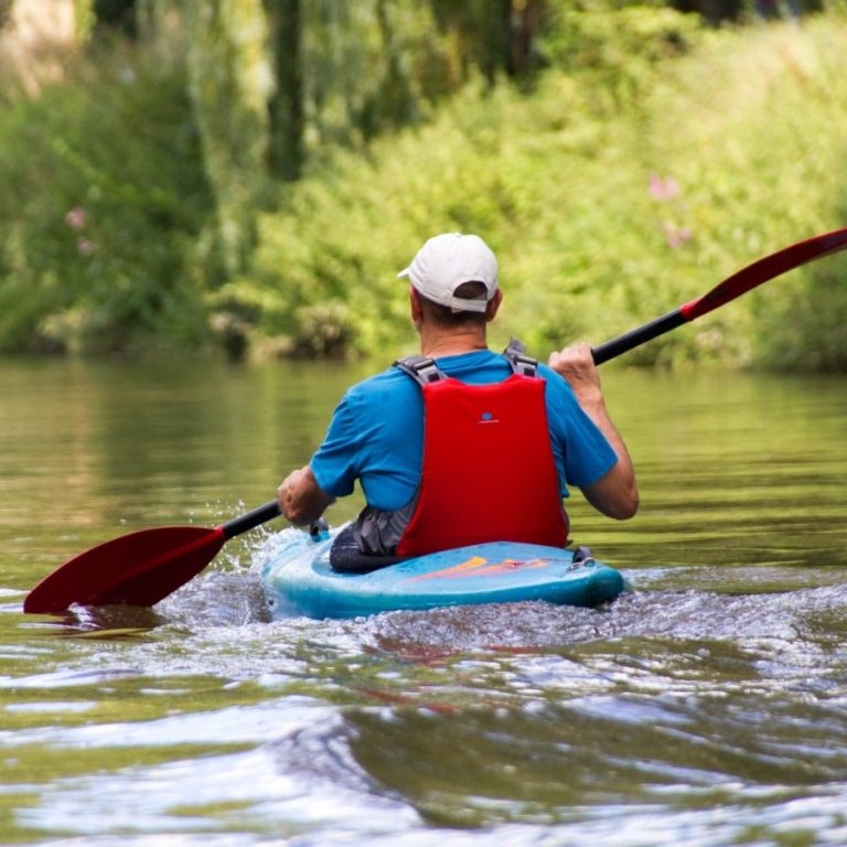 Eine Person paddelt in einem Kajak auf ruhigem Wasser, umgeben von grüner Natur.