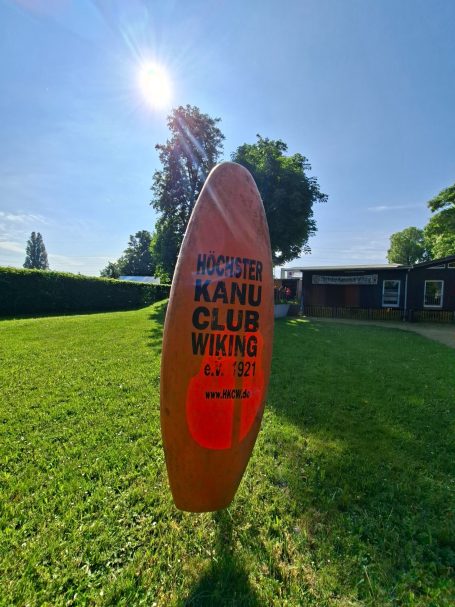 Kajak mit Beschriftung mit Höchster Kanuclub Wiking Kajak mit der Aufschrift "Höchster Kanuclub Wiking", umgeben von grünem Gras und Bäumen.