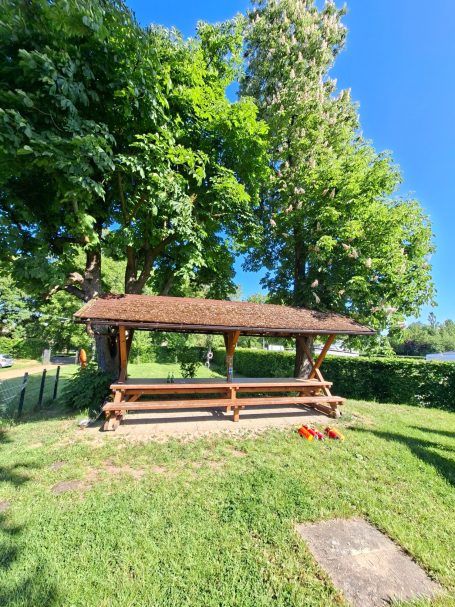 Bootshaus Frankfurt am Main Eine Holzpergola mit Strohdach umgeben von grünen Bäumen und Rasenfläche.