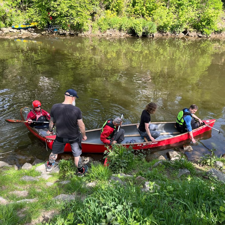 Slalomstangen aufhängen an der Nidda Vier Personen steigen in einen roten Kanadier am Ufer von einem ruhigen Fluss.