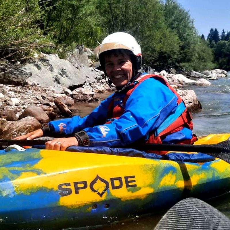 Person im Kanu auf einem Fluss, umgeben von Bäumen und Steinen, lächelt in die Kamera.