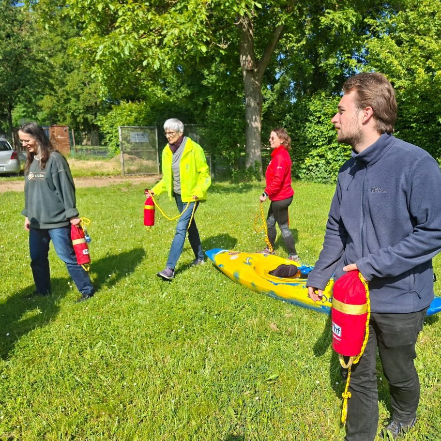Kanu-Sicherheitstraining für Anfänger Gruppe von vier Personen mit Wurfsäcken und einem Boot auf einer grünen Wiese.
