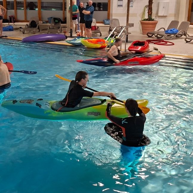 Schwimmbadtraining Zwei Personen im Schimmbadbecken, eine sitzt im Kajak, die andere unterstützt sie beim Üben.