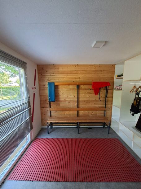 Umkleidekabine Herren im frankfurter Bootshaus des HKCW Ein Raum mit Holzverkleidung, einer Matte und Garderobenhaken an der Wand.