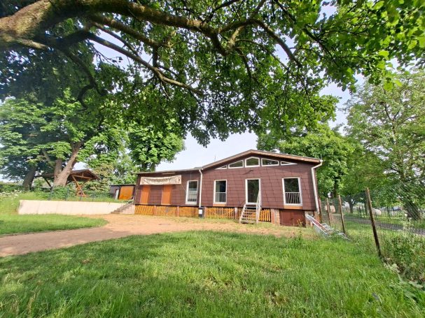 Bootshaus Höchster Kanuclub Wiking e. V. in Frankfurt am Main Rotes Holzhaus mit Veranda, umgeben von grüner Wiese und großen Bäumen.