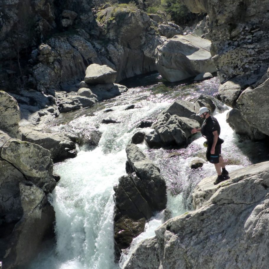 Mann steht an einem Wasserfall in einer felsigen Landschaft.