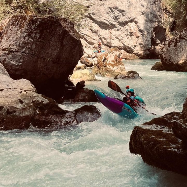 Kajakfahrer paddelt durch eine enge Schlucht mit steilen Felswänden und klarem Wasser.